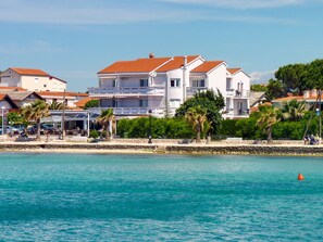 Un hotel costero con fachada blanca, techo de tejas rojas y una pared de piedra a lo largo del paseo marítimo.