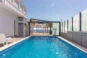 Ein Schwimmbad mit klarem, blauem Wasser, ein weißes Gebäude mit Balkon und Blick aufs Meer.