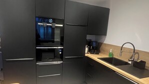 Una cocina moderna con armarios oscuros, horno empotrado, lavamanos y encimera de madera.