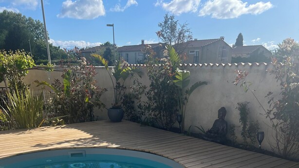 Una piscina con cubierta de madera, rodeada de plantas y una estatua de Buda.