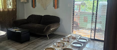 A dining area with a table set for six, a ceiling fan, macramé wall hangings, a sofa, and a view through a glass door.