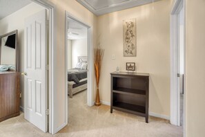 Ein Flur mit einer zurückliegenden Tür zu einem Schlafzimmer, einem Konsolentisch mit einer Vase und einem an der Wand hängenden Bild.