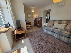 Ein Wohnzimmer mit einer Couch, einem Holztisch, einem Fernseher und einem kleinen Tisch mit einem Laptop.