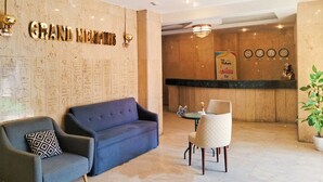 A lobby with a reception desk, a blue sofa, a chair, and a wall with hieroglyphs. - Grand Memphis Single Room (luxor)