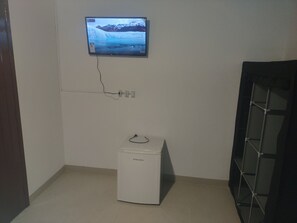 A room with a wall-mounted TV displaying a snowy landscape, a white appliance on the floor, and a door on the left.