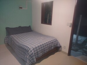 A bedroom with a bed, a window, and a door leading to a balcony.
