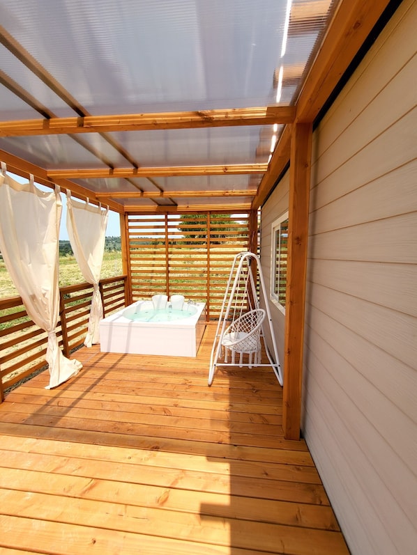 A wooden deck with a hot tub, a swing chair, and a pergola with curtains.