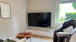 A modern living room with a flat-screen TV, a massage chair, a sofa, and a coffee table. - Black Forest Getaway | Private Sauna, Massage Chair & Views 🌲 (Schönwald im Schwarzwald)