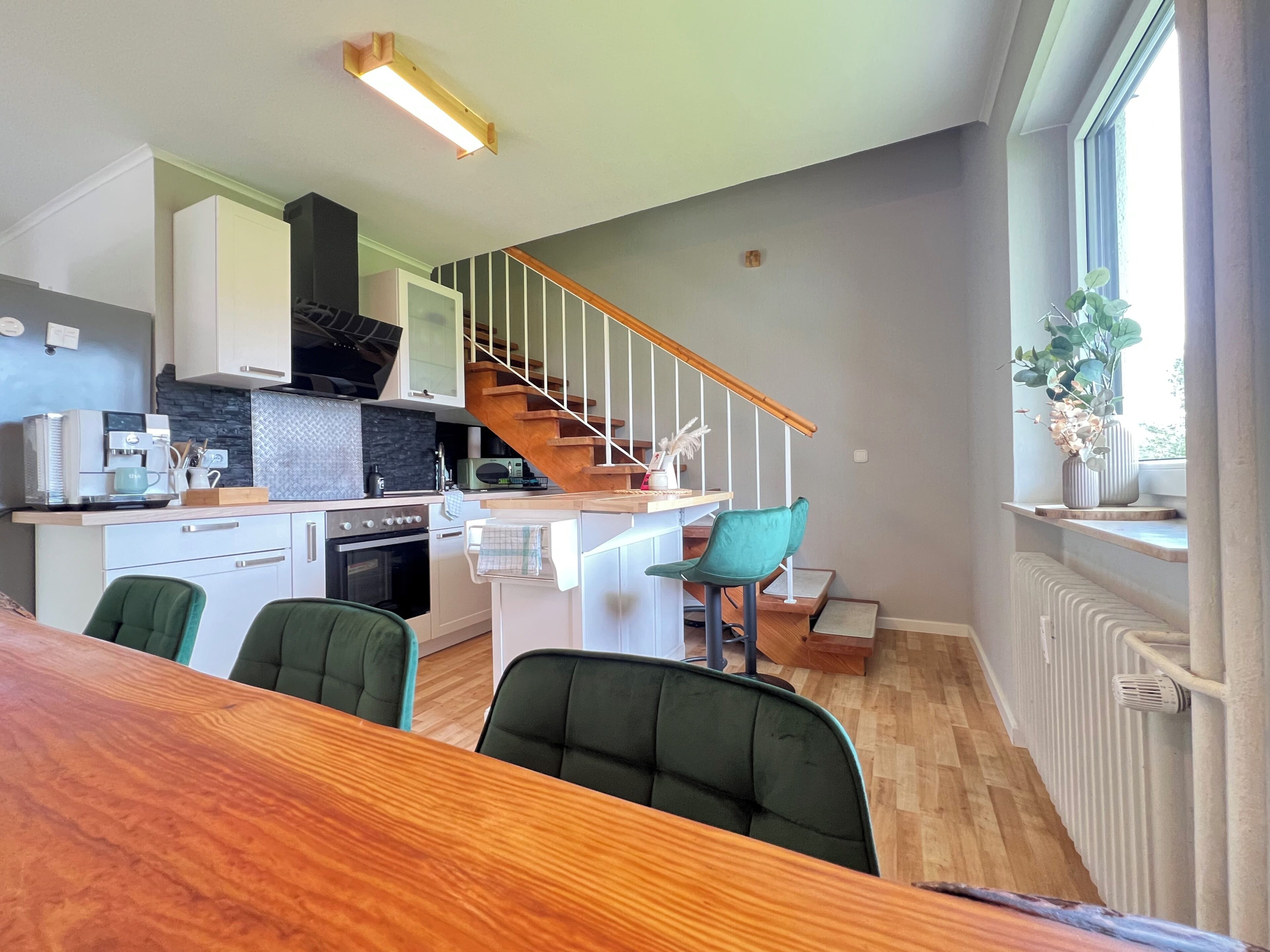 Una cocina moderna con una escalera de madera, sillas verdes y una mesa de comedor.