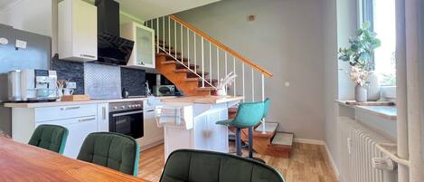 Una cocina moderna con una escalera de madera, sillas verdes y una mesa de comedor.