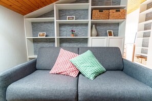 A grey sofa with two pillows, a white shelving unit with baskets, and a stone-textured wall. - Black Forest Getaway | Private Sauna, Massage Chair & Views 🌲 (Schönwald im Schwarzwald)