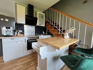 Une cuisine moderne avec des meubles blancs, un plan de travail en bois, un four encastré et un escalier en bois.