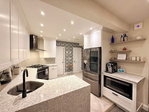 A modern kitchen with white cabinets, a stainless steel refrigerator, a built-in oven, and a granite countertop.