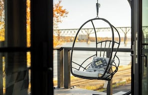 A wicker chair with a cushion on a balcony with a view of a bridge and trees.