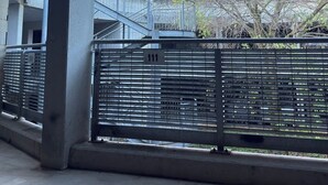 A covered outdoor area with a metal fence, concrete pillars, and a view of a building and trees in the background. - House in Progress (Colle di Val d'Elsa)