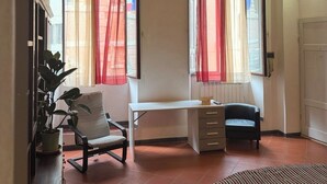 A room with a wooden ceiling, a desk, two chairs, a radiator, and a potted plant. - House in Progress (Colle di Val d'Elsa)