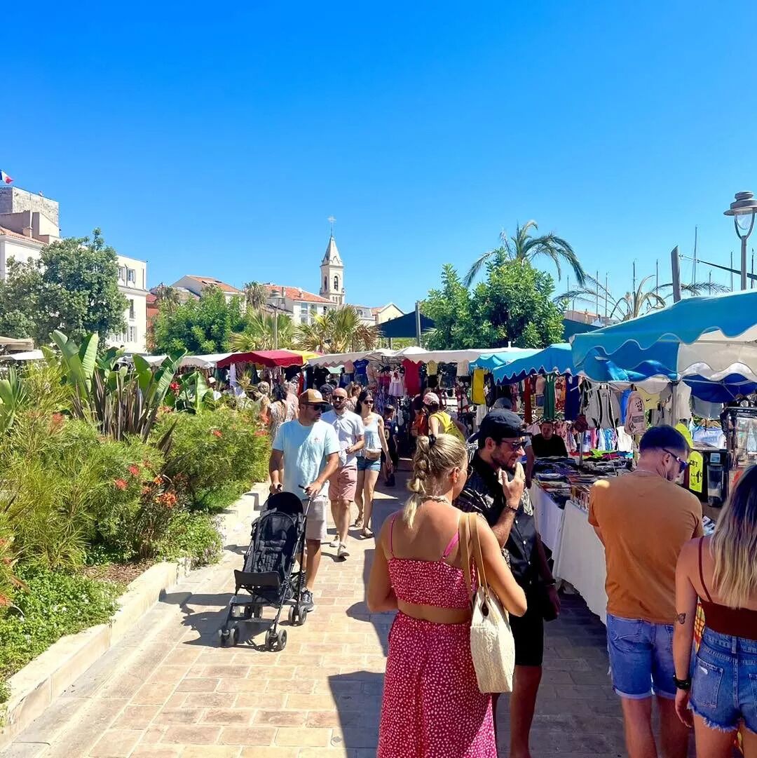 Un vivace mercato all'aperto con persone che passeggiano e venditori che offrono prodotti sotto ombrelli blu e bianchi.