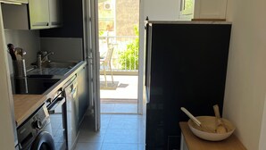 Cozinha compacta com máquina de lavar, pia, armários e um relógio na parede.