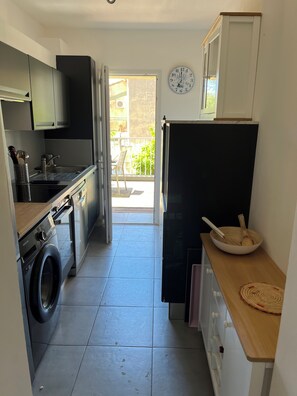 A compact kitchen with a washing machine, a sink, cabinets, and a clock on the wall. - T3 in the heart of the pedestrian zone, 2 steps from the port (Sanary-sur-Mer)