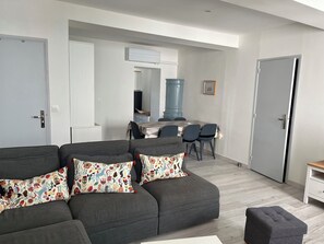 A modern living room with a grey sofa, a dining table with chairs, and a kitchen area in the background. - T3 in the heart of the pedestrian zone, 2 steps from the port (Sanary-sur-Mer)
