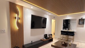 A modern living room with a flat-screen TV, a wooden accent wall, a black entertainment unit, and a coffee table. - The Prestige Long Beach/ On Site Free Parking (Long Beach)