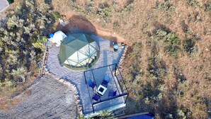 Vista aerea di un campeggio con una tenda circolare, un tavolo da pranzo con sedie e una piccola area salotto all'aperto.