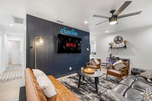 Uma sala de estar moderna com uma parede de destaque azul escuro, TV fixada, ventilador de teto e lareira.