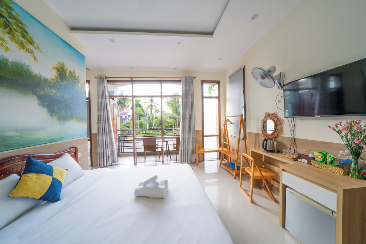 A hotel room with a bed, a desk, a television, and a view of the outdoors.