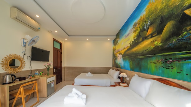 A hotel room with a bed, a desk with a chair, a TV, and a painting on the wall. - New Moon Villa (Hoi An)