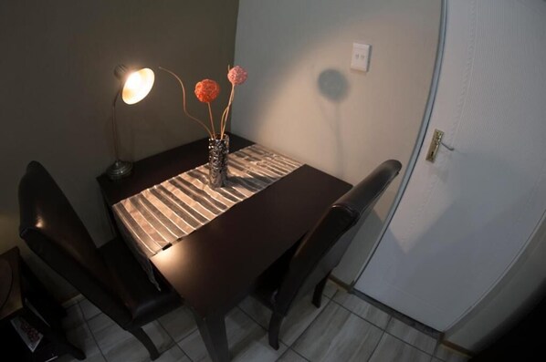 A dining table with chairs, a lamp, and a vase with flowers. - ARISTA GUESTHOUSE (Bloemfontein)