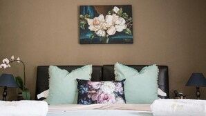 Een hotelkamer met een bed, twee kussens, een schilderij, een lamp en een plant.