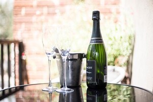 A bottle of wine, two glasses, and a metal bucket on a glass table.
