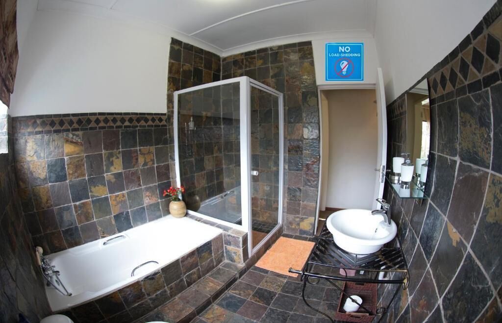 A bathroom with a shower, a bathtub, a sink, and a 'No Load-Shedding' sign.