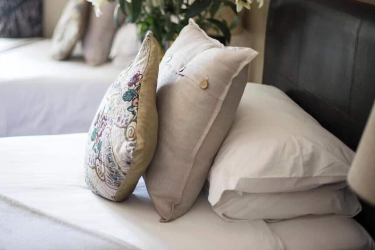 A bed with beige pillows and a decorative pillow, a vase with flowers, and a dark headboard.