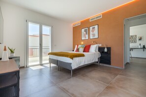 A modern bedroom with a bed, a nightstand, a potted plant, and a sliding glass door to a balcony. - Flamingo's Way: modern penthouse, large terrace, stunning view of sea and city (Cagliari)
