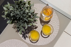 Ein Tisch mit einer gewebten Tischmatte, zwei Gläsern Orangensaft und einem Blumentopf.