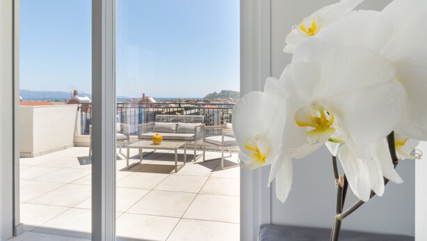 Un balcón con vista al mar, una orquídea blanca y una zona de estar con mesa y sillas.