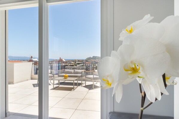 Ein Balkon mit Meerblick, eine weiße Orchidee und eine Sitzgelegenheit mit Tisch und Stühlen.