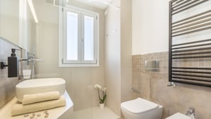 Un baño moderno con inodoro, bidé, lavamanos y un espejo grande.