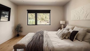 A bedroom with a bed, a bench, a window, and a wall-mounted lamp. - Tilden House | Designer Pool Home in West LA (Los Angeles)