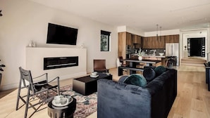 A modern living room with a flat-screen TV, a fireplace, a sofa, and a dining area with wooden cabinets. - Tilden House | Designer Pool Home in West LA (Los Angeles)