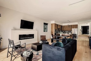 Ein modernes Wohnzimmer mit Flachbildfernseher, Kamin, einer Couch und einem Essbereich mit Holzsäulen.