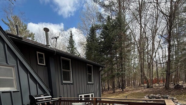 A deck with outdoor furniture, a grill, and a cabin in a wooded area. - The Remington House - Pet friendly, hot tub, and on ATV trails (Woodruff)