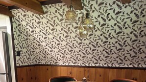 A dining area with a round wooden table, four green upholstered chairs, a patterned wallpaper, and hanging pendant lights. - The Remington House - Pet friendly, hot tub, and on ATV trails (Woodruff)