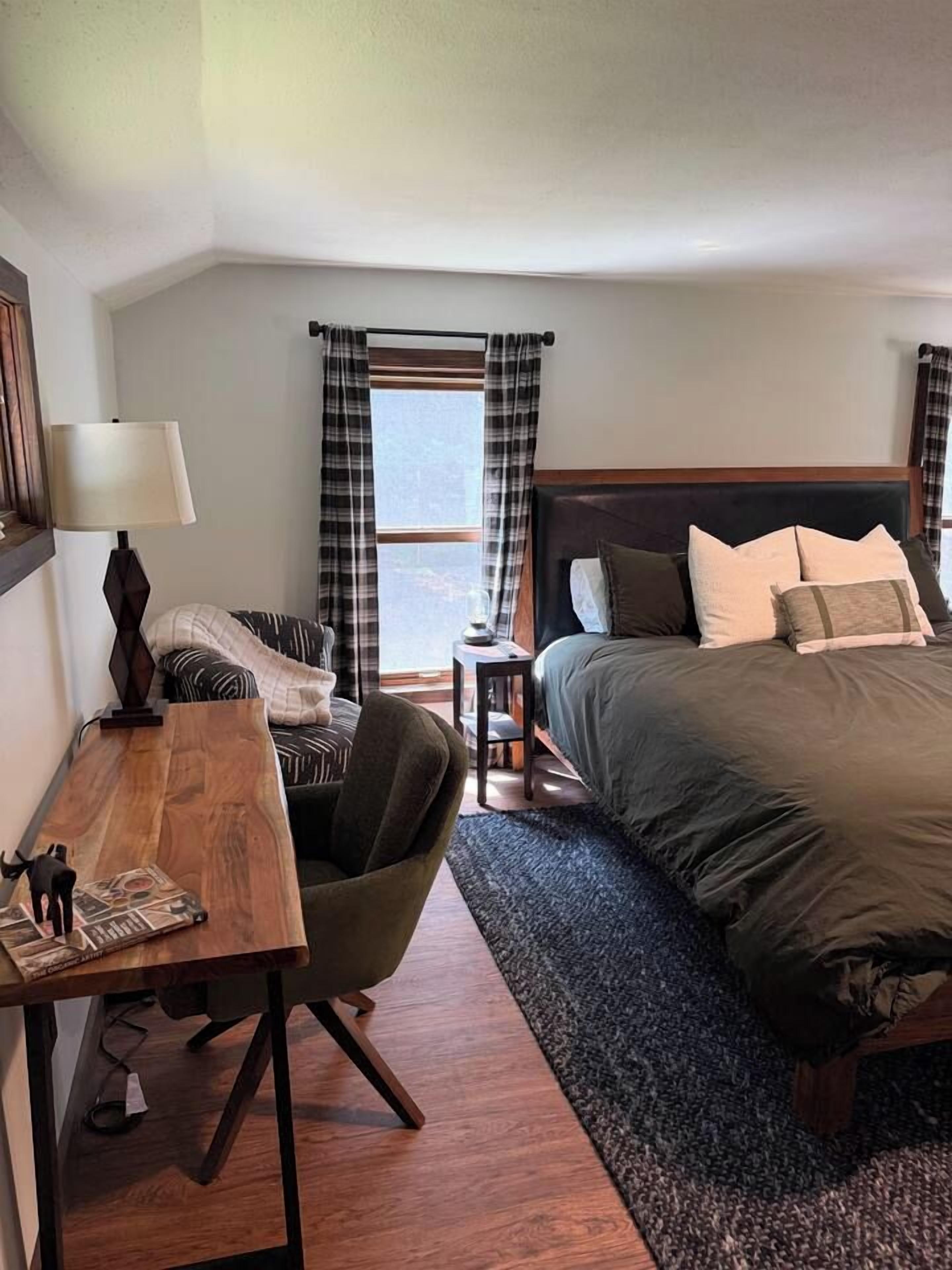 A hotel room with a bed, a desk, a chair, and a window with curtains.