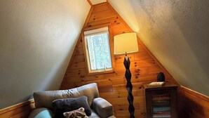 A cozy attic bedroom with a sloped ceiling, a window, a lamp, a small cabinet, and a sofa with pillows. - The Remington House - Pet friendly, hot tub, and on ATV trails (Woodruff)