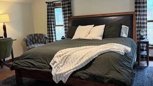 A bedroom with a bed, a bedside table, a lamp, a chair, and a window with curtains. - The Remington House - Pet friendly, hot tub, and on ATV trails (Woodruff)