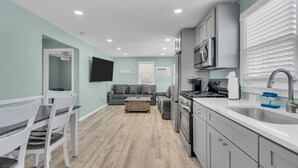 A modern kitchen with a built-in oven, a sink, and a dining area with white chairs and a table. - Paxley`s: 2BR Spacious Beach Haven (Seaside Heights)