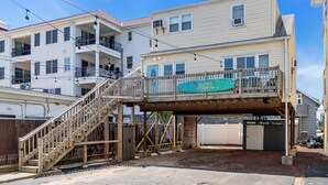 A multi-story building with a wooden staircase leading to a balcony, a sign welcoming to Hiloport Ave, and a garage door. - Paxley`s: 2BR Spacious Beach Haven (Seaside Heights)
