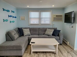 Ein Wohnzimmer mit grauem Ecksofa, einem weißen Couchtisch, einem Flachbildfernseher und Wandbildern von Fischen.